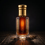 Amber Oud, unisex — alcohol-free oud oil (oudh) by Flora Five: deep amber oil in a gold-capped bottle on weathered dark wood with oud chips