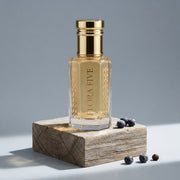 Burberry Hero inspired attar for men — alcohol-free perfume oil by Flora Five: pale gold oil in a gold-capped bottle on a weathered wood block with juniper