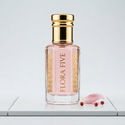 Byredo Rose of No Man's Land inspired unisex attar — alcohol-free perfume oil by Flora Five: pale pink oil on white tile with a rose petal, pink peppercorns