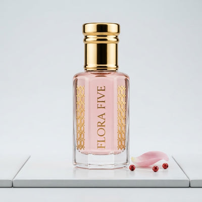 Byredo Rose of No Man's Land inspired unisex attar by Flora Five — alcohol-free perfume oil: gold-capped bottle of pale pink oil on a white tile with a rose petal and pink peppercorns – 3, 6 and 12 ml