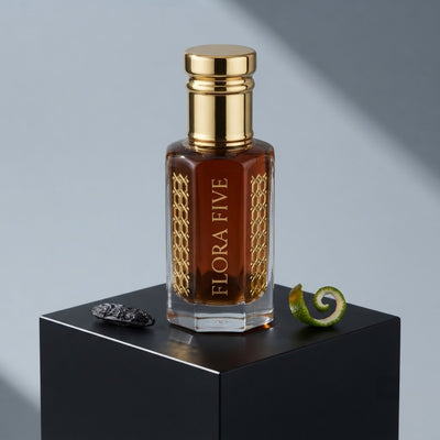 Carolina Herrera Bad Boy inspired attar for men by Flora Five — alcohol-free perfume oil: gold-capped bottle of deep red-brown oil on a black plinth with a tonka bean and lime peel – 3, 6 and 12 ml