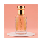 Escada Kiss Land inspired attar for women — alcohol-free perfume oil by Flora Five: peach oil in a gold-capped bottle on a white plinth against coral pink