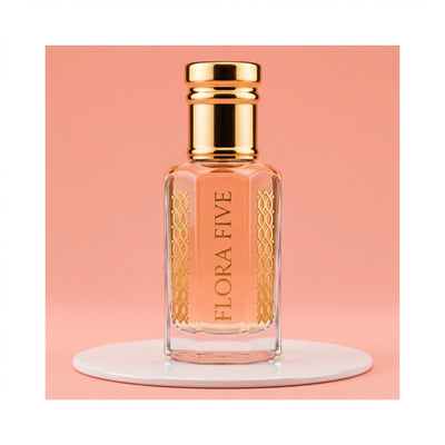 Escada Kiss Land inspired attar for women — alcohol-free perfume oil by Flora Five: peach oil in a gold-capped bottle on a white plinth against coral pink