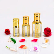 Dior J'adore inspired attar for women — alcohol-free perfume oil by Flora Five: three empty gold-trimmed bottles with red roses, petals and white flowers