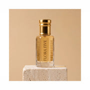 Sandal Aura Attar, unisex — alcohol-free attar oil by Flora Five: pale golden oil in a gold-capped bottle on a travertine block, sand-beige backdrop