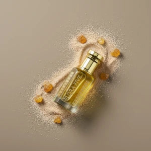 Flora Five's Perfume bottle with gold cap and gold liquid on a beige background surrounded by amber and powder.
