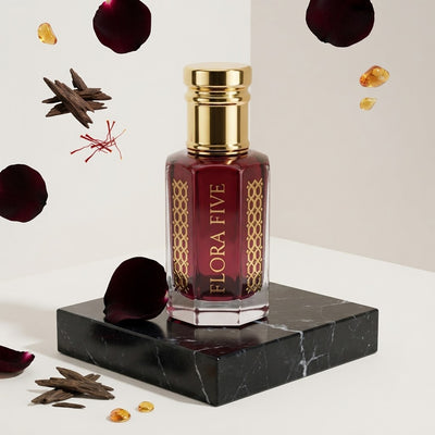 Black Rose Attar by Flora Five — gold-capped bottle of deep garnet oil on black marble with floating rose petals, oud chips and saffron – 3, 6 and 12 ml