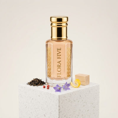 Burberry The Beat inspired attar for women by Flora Five — alcohol-free perfume oil: gold-capped bottle of pale peach oil on a white stone block with tea leaves, bellflowers and pink pepper – 3, 6 and 12 ml