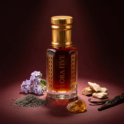 Deer Musk Attar by Flora Five — gold-capped bottle of deep amber oil on burgundy with lilac, musk grains and wood chips – 3, 6 and 12 ml