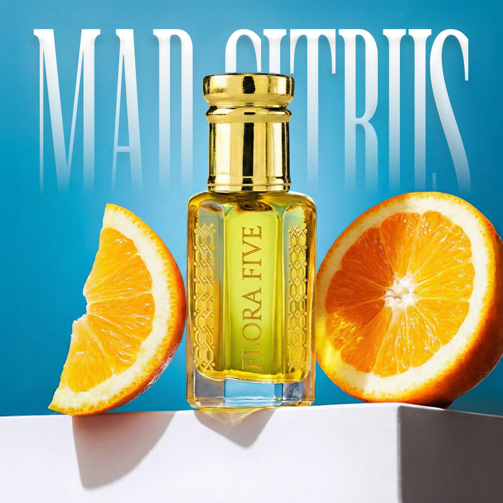 Mad Citrus attar by Flora Five in a luxury glass perfume oil bottle with fresh orange slices, citrus notes, and a modern blue studio background