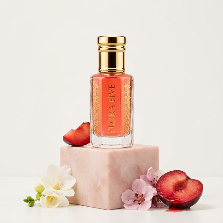 Victoria's Secret Pure Seduction Inspired Attar by Flora Five — gold-capped bottle of coral-red oil on a pink stone block with a blood plum, freesia and pink blossoms – 3, 6 and 12 ml