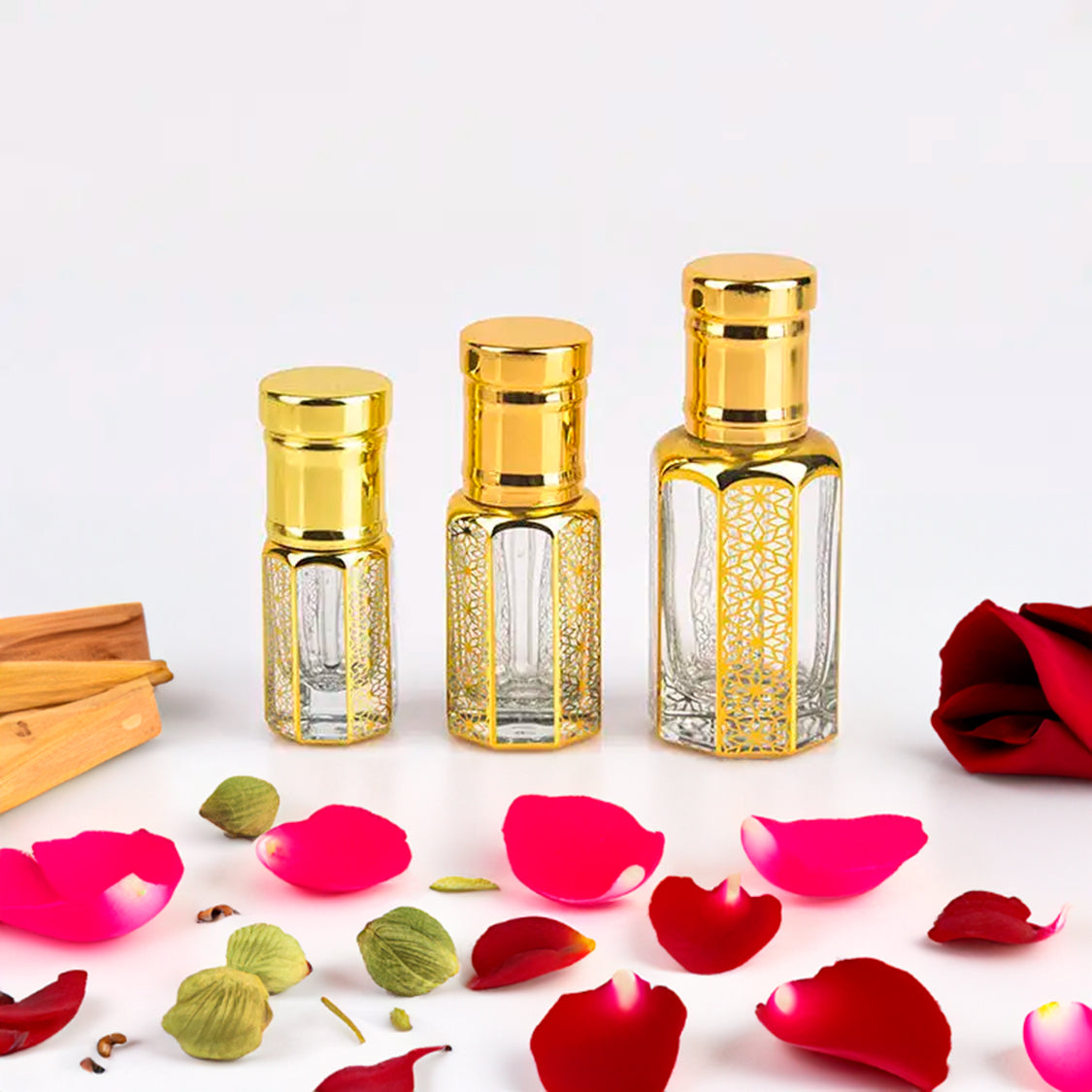 Flora Five White Arabian Oudh fragrance attar bottles in three sizes with intricate golden designs, surrounded by rose petals, cardamom, and sandalwood. This long-lasting attar offers a sweet floral and woody fragrance, perfect for those seeking a luxurious and enduring scent experience.
