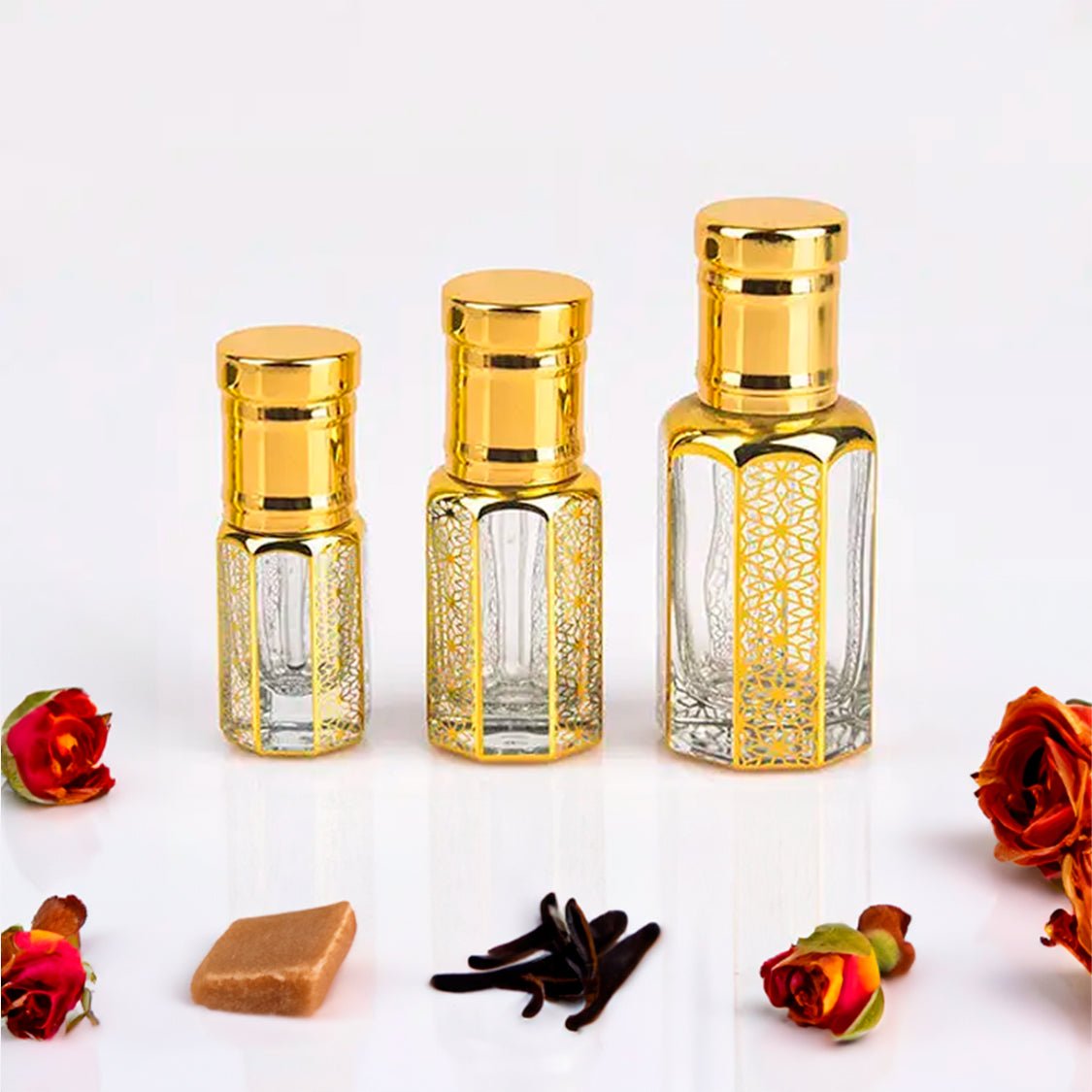 Amir Al Oudh by Flora Five fragrance attar bottles in three sizes with intricate golden designs, surrounded by roses, vanilla beans, and a caramel piece. This long-lasting attar offers a sweet musky and woody fragrance, perfect for those seeking a luxurious and enduring scent experience.
