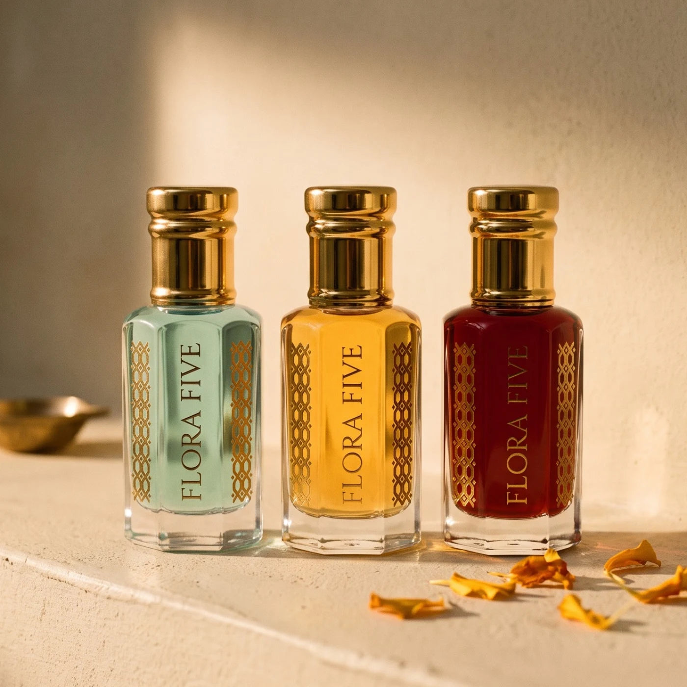 Build Your Trio of attars and ouds by Flora Five — three alcohol-free oils in aqua, golden and garnet bottles on an ivory ledge with marigold petals
