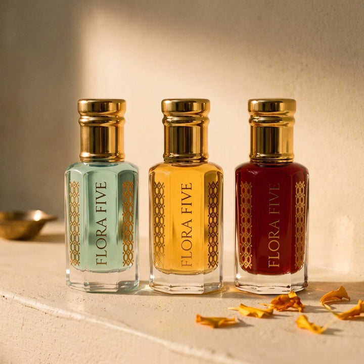 Build Your Trio of attars and ouds by Flora Five — three alcohol-free oils in aqua, golden and garnet bottles on an ivory ledge with marigold petals