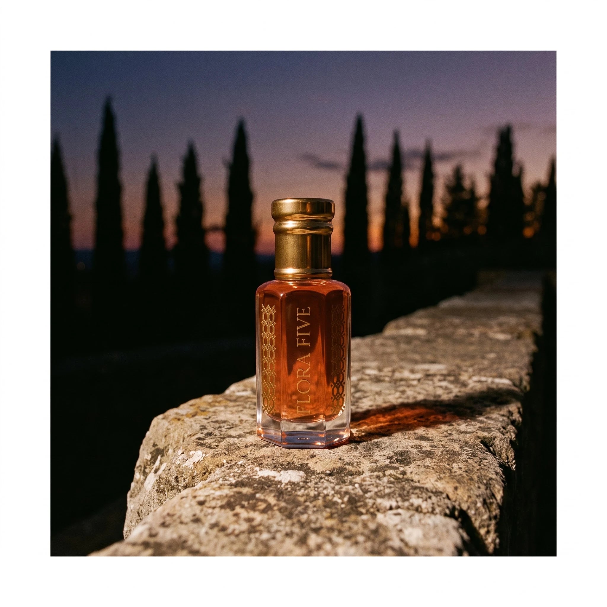 Diptyque Tam Dao inspired attar by Flora Five — bottle on an old stone wall with cypress trees silhouetted at dusk