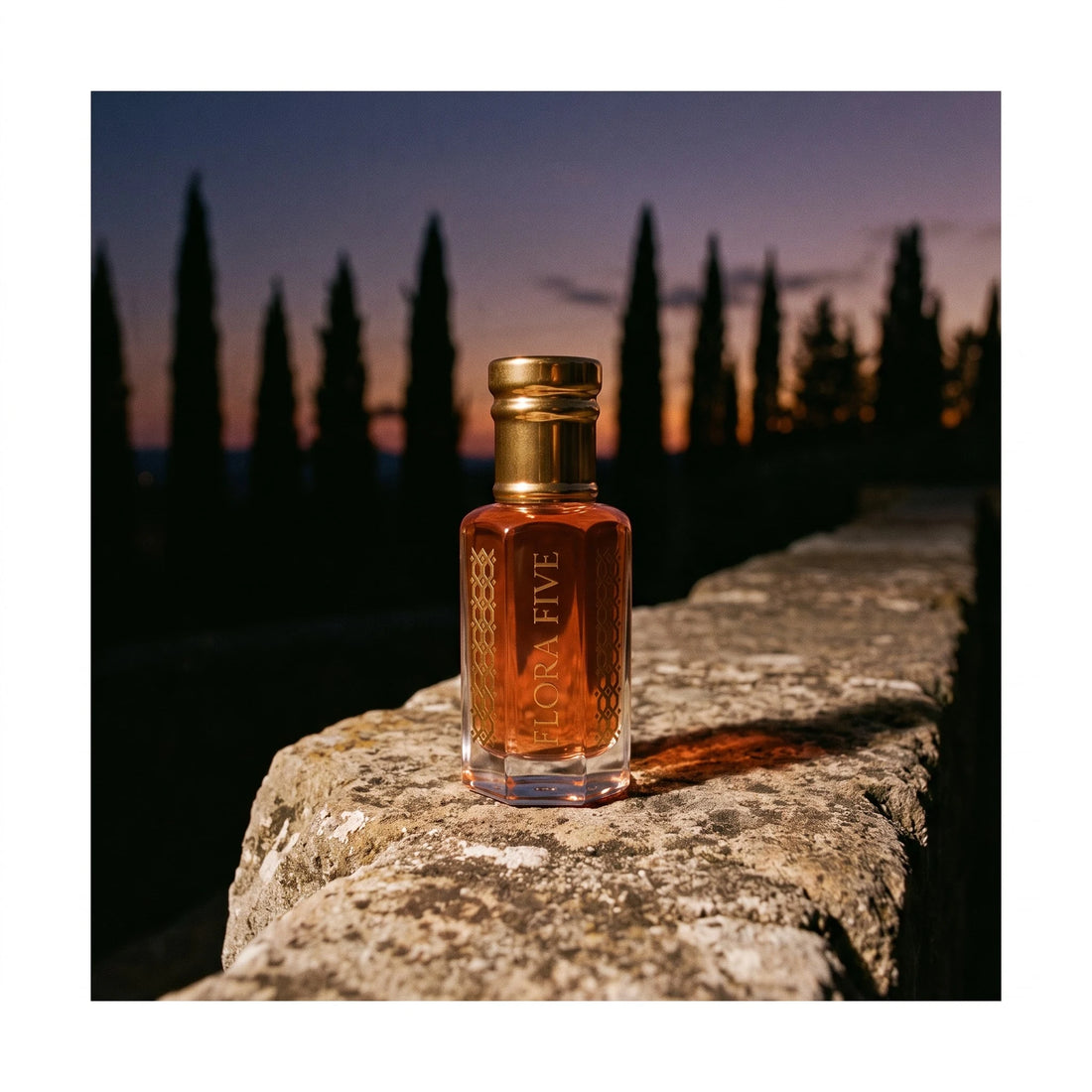 Diptyque Tam Dao inspired attar by Flora Five — bottle on an old stone wall with cypress trees silhouetted at dusk
