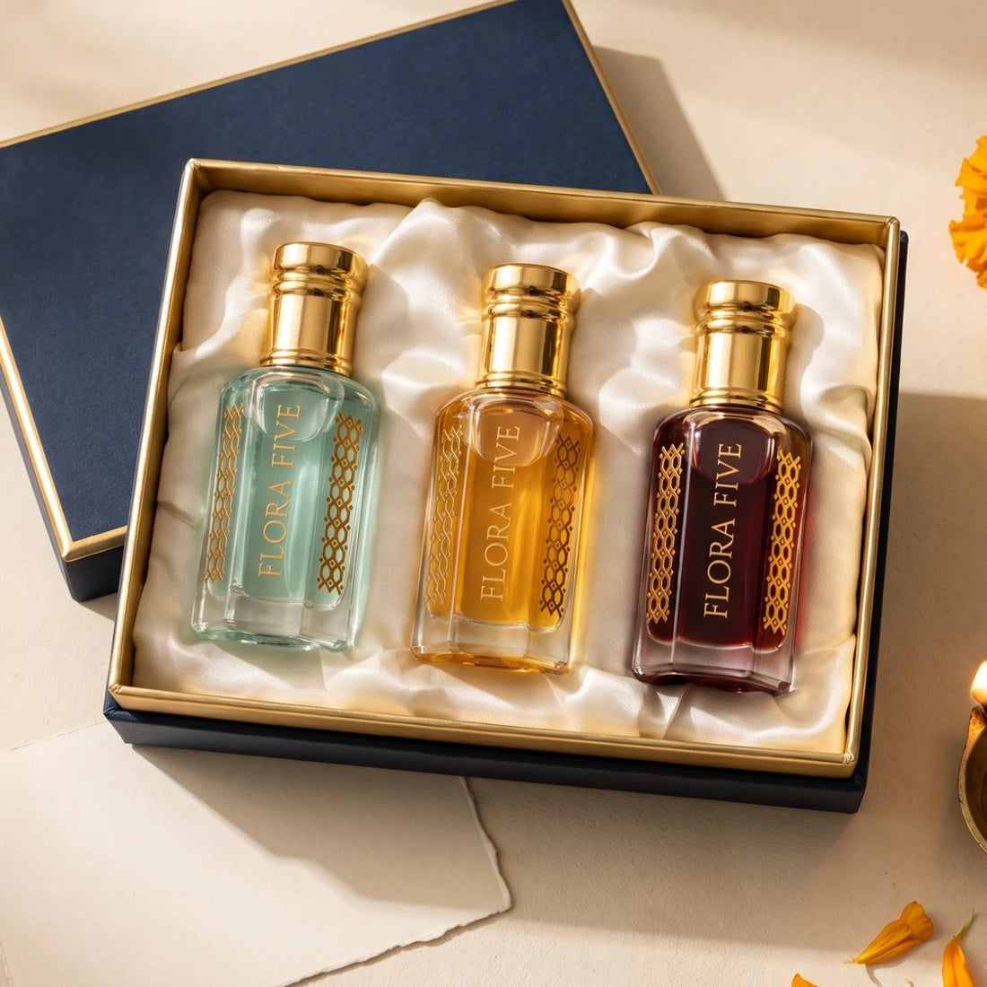 Diwali Gift Box by Flora Five — three 6 ml alcohol-free attar and oud bottles in aqua, gold and ruby on ivory satin in a navy and gold box with marigolds