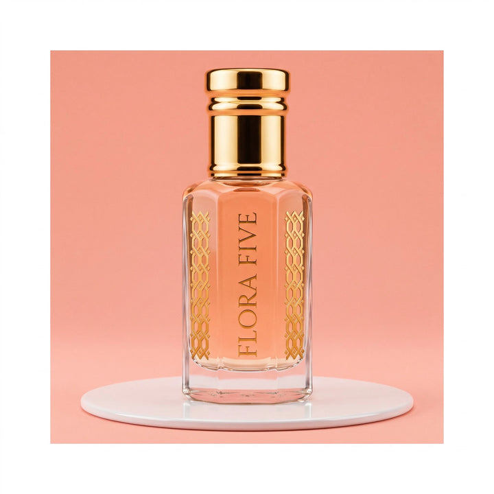 Escada Kiss Land inspired attar for women — alcohol-free perfume oil by Flora Five: peach oil in a gold-capped bottle on a white plinth against coral pink