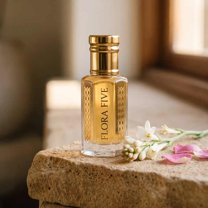Madhaavi attar by Flora Five: honey-gold oil bottle on sandstone with tuberose and rose petals