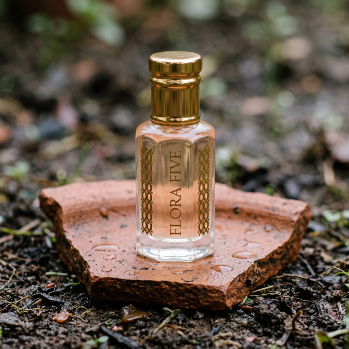 Mitti Attar (petrichor) by Flora Five: pale peach oil bottle on a terracotta shard on damp earth with raindrops
