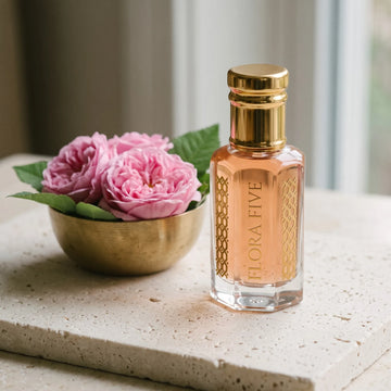 Taifi Rose Attar, unisex — alcohol-free attar oil by Flora Five: peach-pink oil on travertine beside pink damask roses in a brass bowl