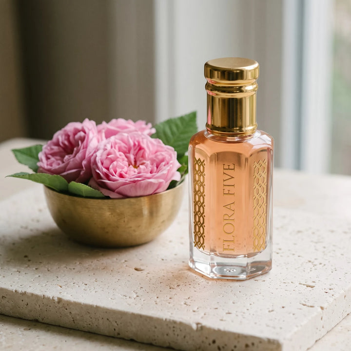 Taifi Rose attar by Flora Five: rose-amber oil bottle on cream stone with damask roses in a brass bowl