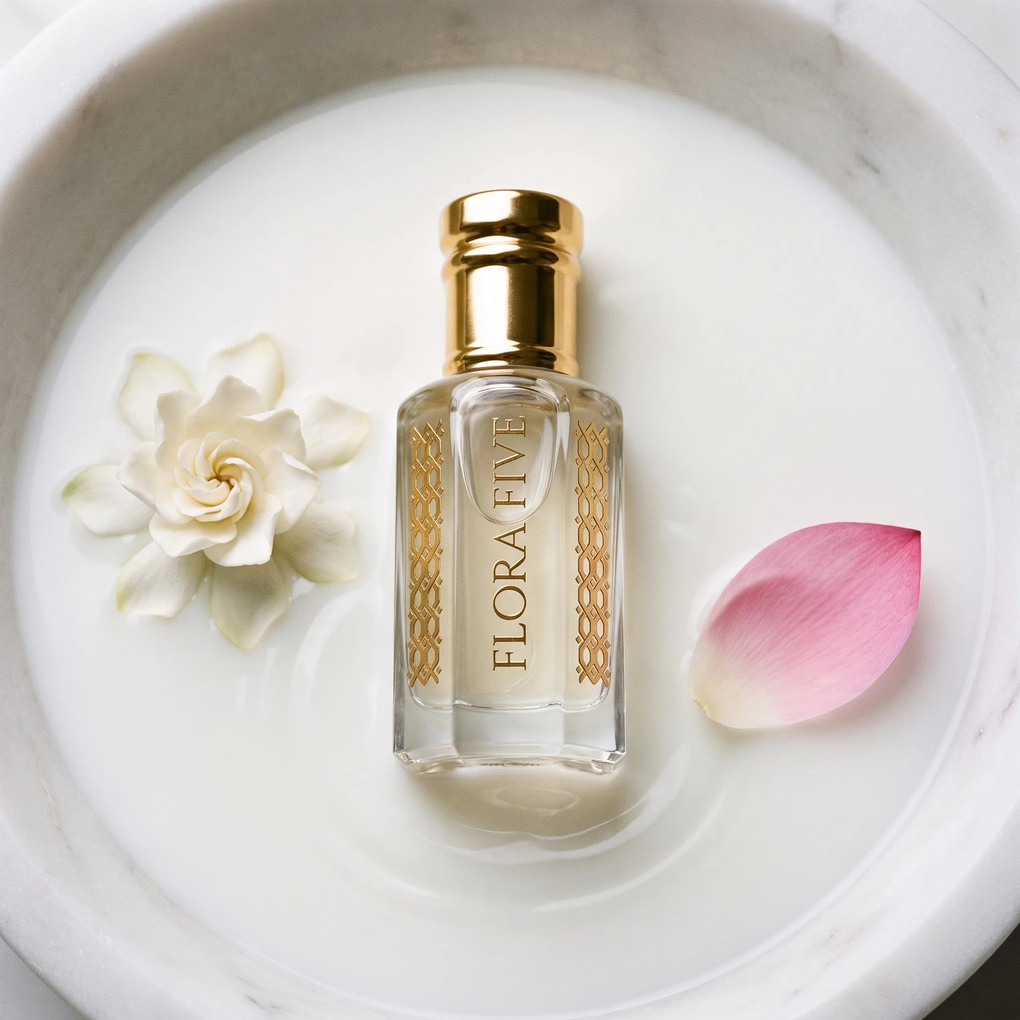 White Firdaus Attar by Flora Five — bottle in a marble basin of milk with a gardenia and a pink lotus petal